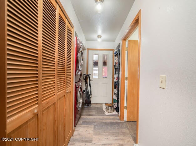 hallway featuring a textured ceiling, stacked washer and clothes dryer, and hardwood / wood-style flooring