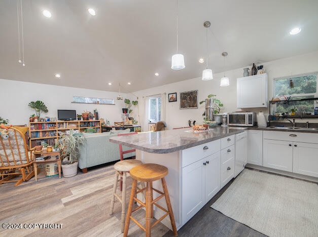 kitchen featuring light hardwood / wood-style floors, dark stone counters, white cabinetry, sink, and pendant lighting