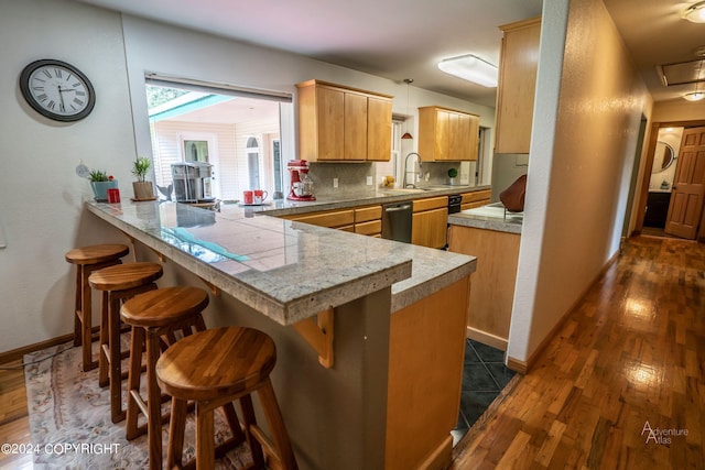 kitchen featuring kitchen peninsula, dishwasher, dark wood-type flooring, backsplash, and a breakfast bar area