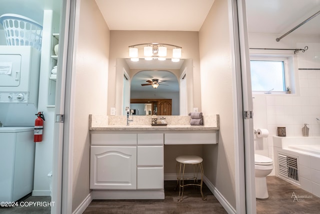 bathroom featuring ceiling fan, vanity with extensive cabinet space, stacked washer and clothes dryer, and toilet