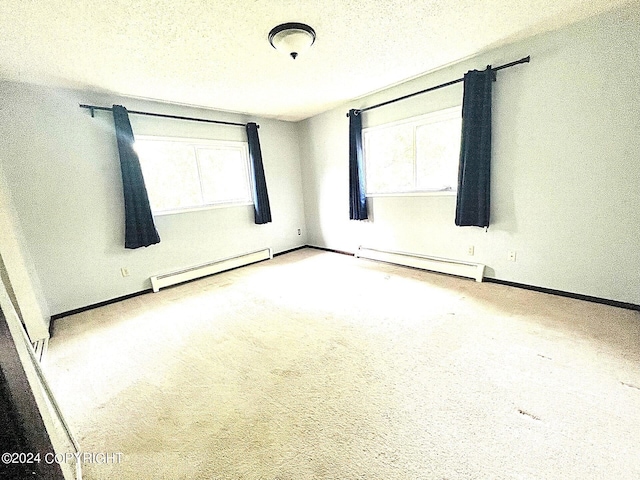 carpeted spare room with baseboard heating, a textured ceiling, and a healthy amount of sunlight