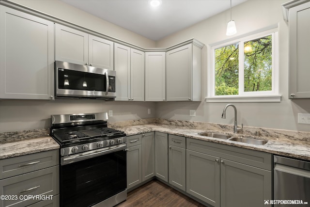 kitchen with appliances with stainless steel finishes, gray cabinets, hanging light fixtures, sink, and dark hardwood / wood-style flooring