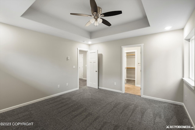 unfurnished bedroom featuring a closet, carpet floors, a tray ceiling, ceiling fan, and a walk in closet