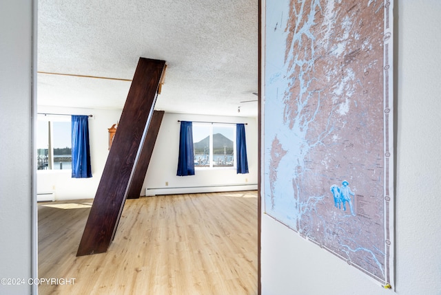 hallway featuring light hardwood / wood-style flooring, baseboard heating, and a textured ceiling