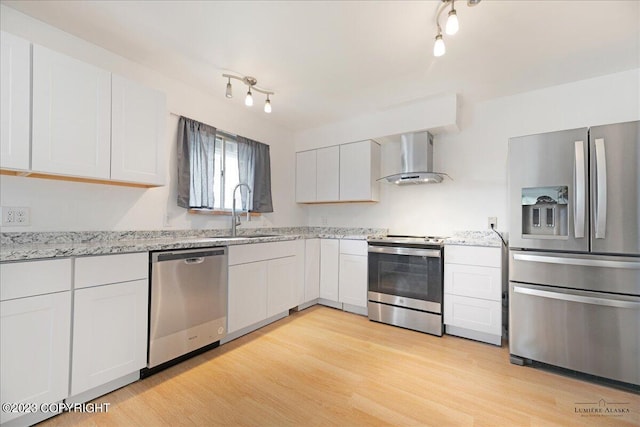 kitchen with light hardwood / wood-style flooring, stainless steel appliances, sink, rail lighting, and wall chimney exhaust hood