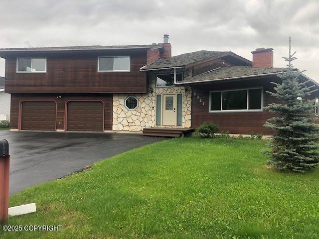 9511 Albatross Dr, Anchorage, AK 99502 - split level home featuring a garage, a chimney, driveway, a front lawn, and stone siding