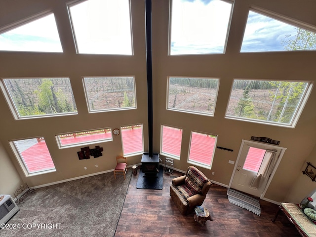 living room featuring a wood stove, a high ceiling, baseboards, and wood finished floors