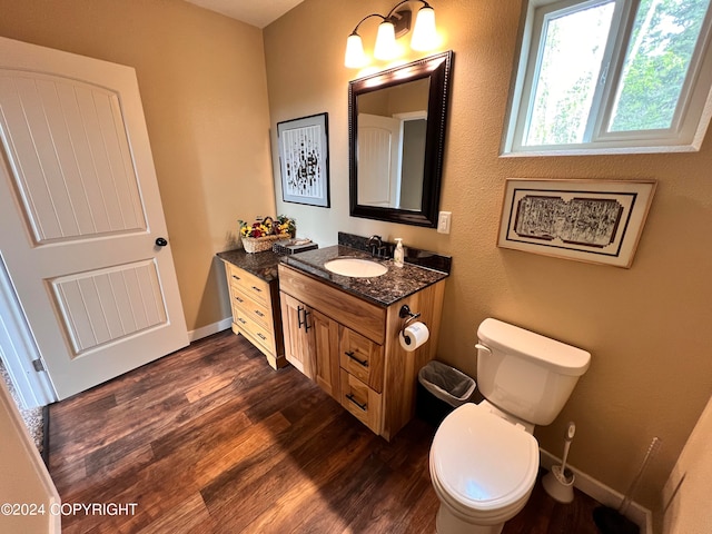 half bath featuring vanity, wood finished floors, toilet, and baseboards