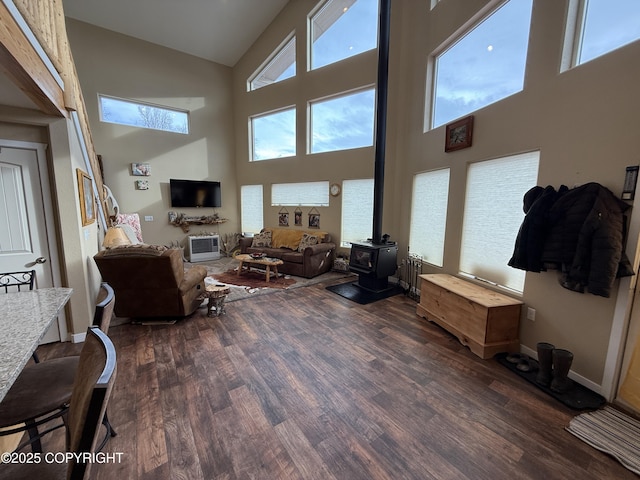 living room featuring a wood stove, dark wood-style floors, baseboards, and high vaulted ceiling