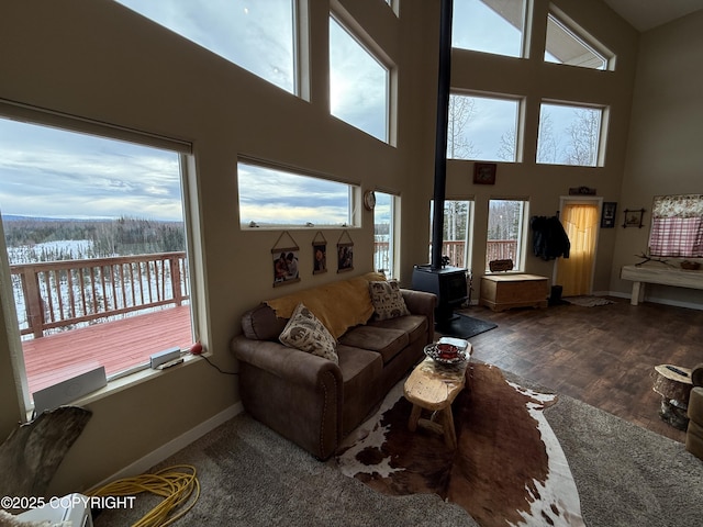 living room featuring a wood stove, a high ceiling, baseboards, and wood finished floors