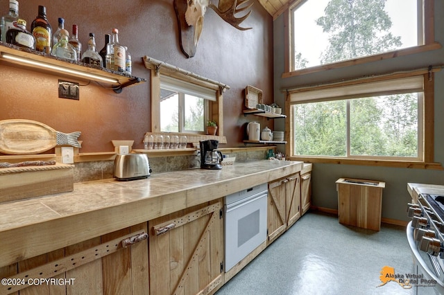 kitchen with tile countertops, a towering ceiling, open shelves, and stainless steel range with gas stovetop