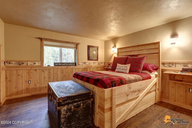 bedroom with a wainscoted wall, wooden walls, hardwood / wood-style floors, and a textured ceiling