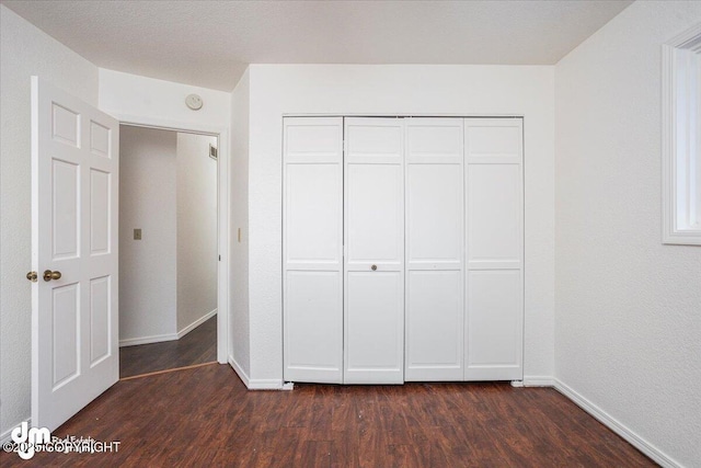 unfurnished bedroom featuring dark wood-style floors, a closet, and baseboards