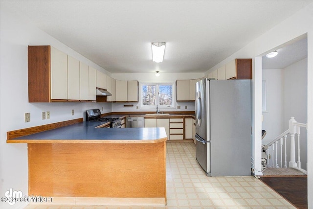 kitchen with under cabinet range hood, a peninsula, a sink, appliances with stainless steel finishes, and light floors