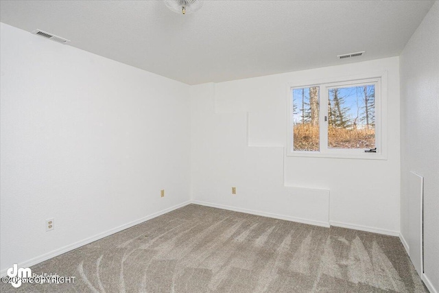 spare room featuring carpet floors, visible vents, a textured ceiling, and baseboards