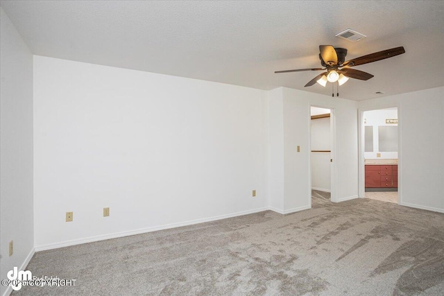 empty room with a textured ceiling, light colored carpet, a ceiling fan, baseboards, and visible vents