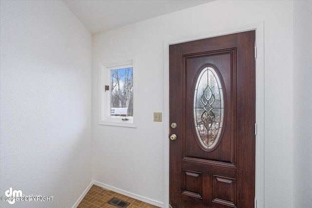 foyer entrance with brick floor, visible vents, and baseboards