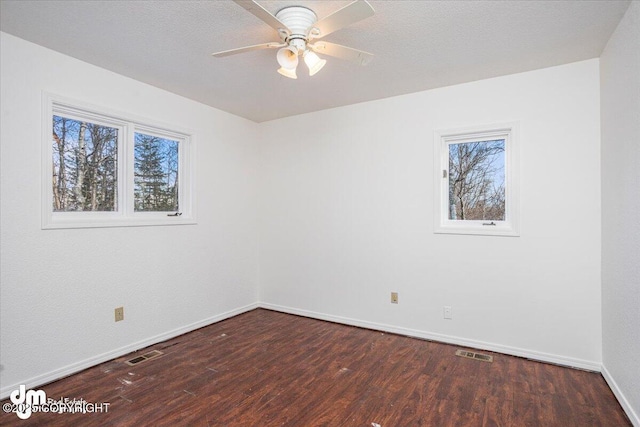 empty room with dark wood-type flooring, visible vents, baseboards, and a ceiling fan