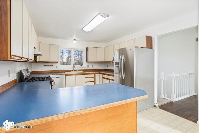 kitchen featuring under cabinet range hood, stainless steel appliances, a peninsula, a sink, and light floors