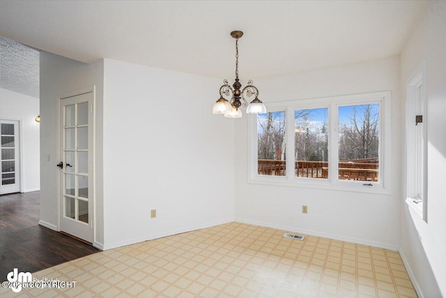 spare room with a textured ceiling, a notable chandelier, visible vents, baseboards, and tile patterned floors