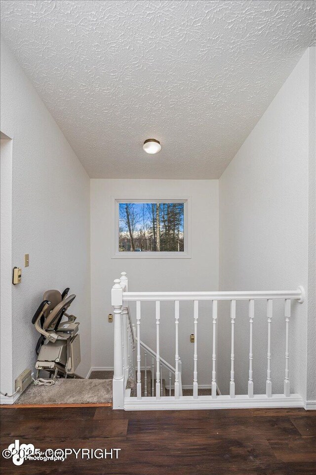 staircase featuring a textured ceiling, wood finished floors, and baseboards