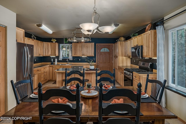 kitchen with light brown cabinetry, hanging light fixtures, stainless steel appliances, and sink