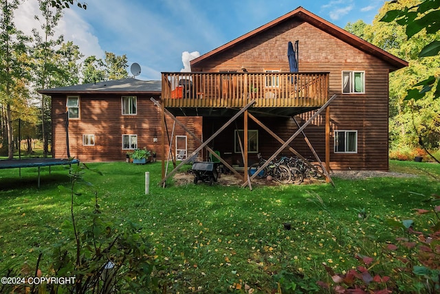 rear view of property featuring a trampoline, a lawn, and a deck