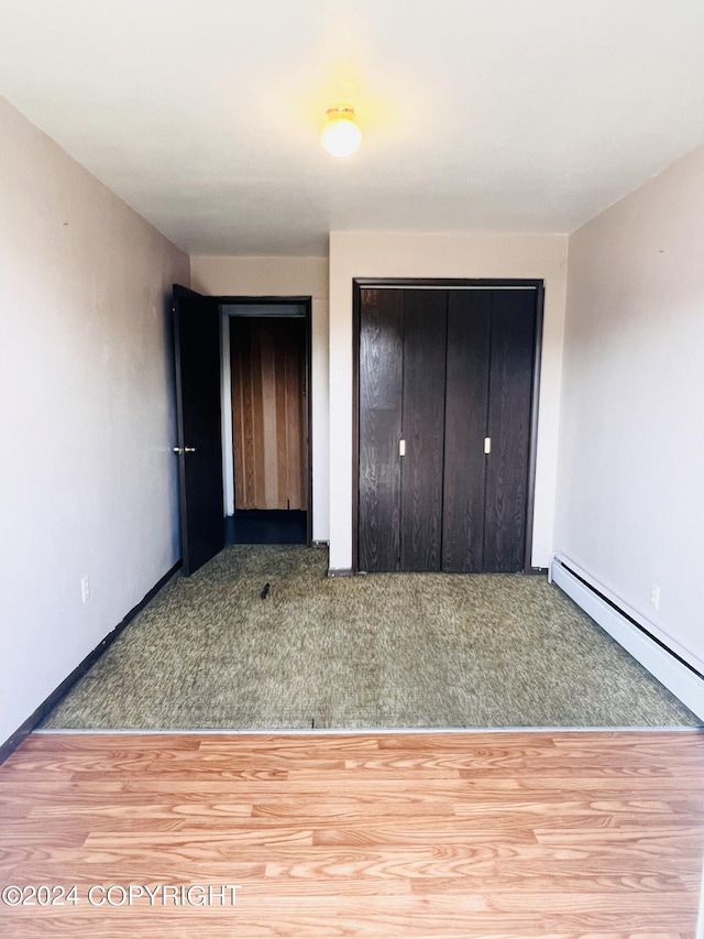 unfurnished bedroom with a closet, a baseboard heating unit, and carpet floors