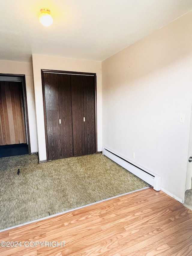 unfurnished bedroom with a closet, hardwood / wood-style floors, and a baseboard radiator