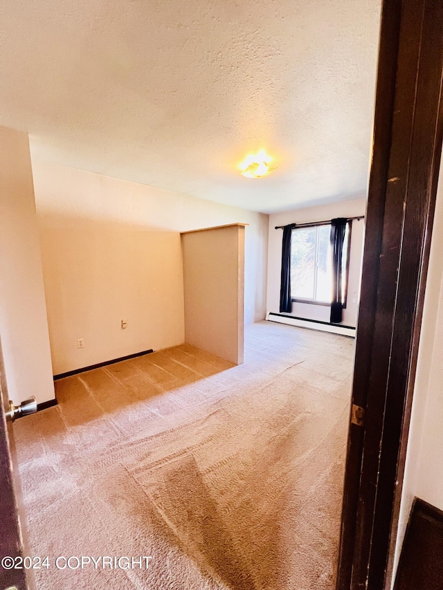 spare room with light carpet, a baseboard heating unit, and a textured ceiling