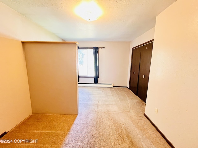 empty room featuring light carpet, a baseboard radiator, and a textured ceiling