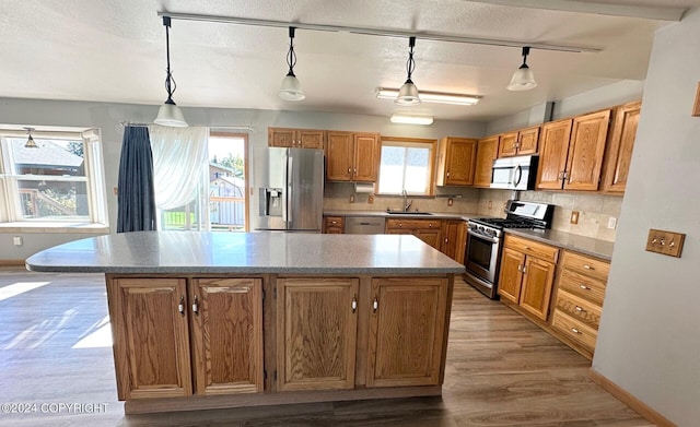 kitchen with stainless steel appliances, hardwood / wood-style floors, a kitchen island, and hanging light fixtures