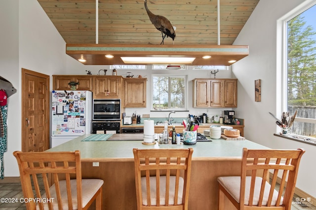 kitchen featuring a kitchen bar, wood ceiling, white refrigerator, black oven, and stainless steel microwave