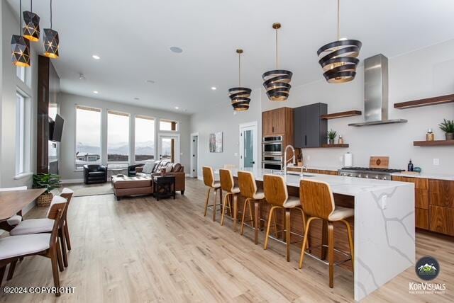 kitchen with wall chimney range hood, light hardwood / wood-style flooring, double oven, a large island, and sink