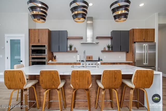 kitchen with a kitchen island with sink, a breakfast bar area, light wood-type flooring, appliances with stainless steel finishes, and range hood