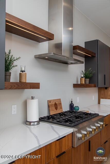 kitchen featuring wall chimney range hood, stainless steel gas stovetop, and light stone counters