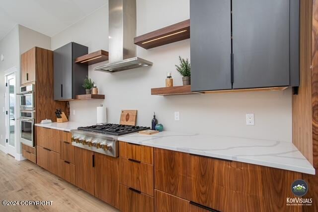 kitchen featuring appliances with stainless steel finishes, light stone countertops, wall chimney exhaust hood, and light hardwood / wood-style flooring