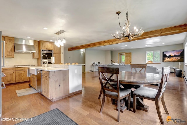 kitchen featuring wall chimney exhaust hood, decorative light fixtures, a kitchen island with sink, and beam ceiling