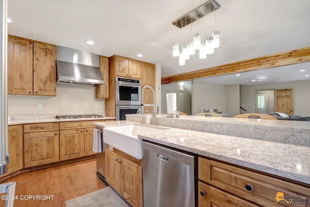 kitchen featuring decorative light fixtures, light hardwood / wood-style floors, stainless steel appliances, light stone countertops, and wall chimney exhaust hood