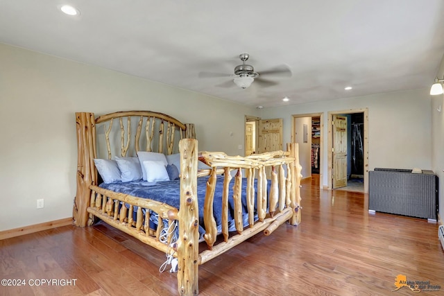 bedroom featuring ceiling fan, a walk in closet, and wood-type flooring