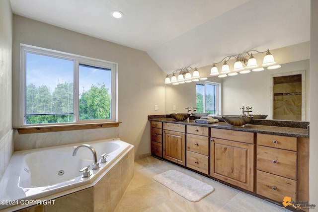 bathroom with tiled tub, vaulted ceiling, vanity, and tile patterned floors