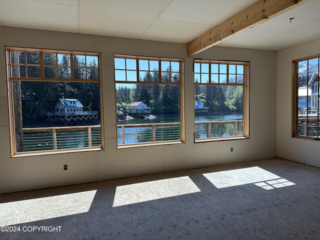 spare room with carpet flooring, a healthy amount of sunlight, a water view, and beam ceiling