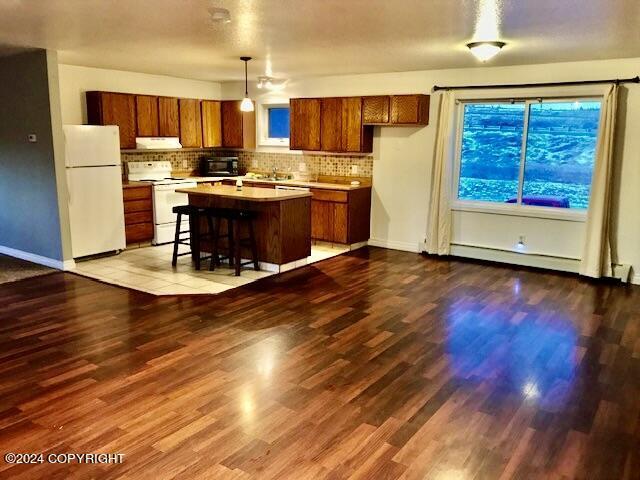 kitchen with a breakfast bar, white appliances, hardwood / wood-style floors, a center island, and hanging light fixtures