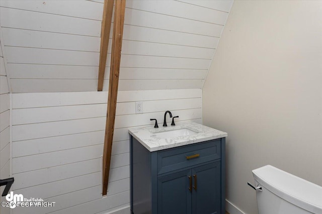 bathroom with wood walls, vanity, lofted ceiling, and toilet