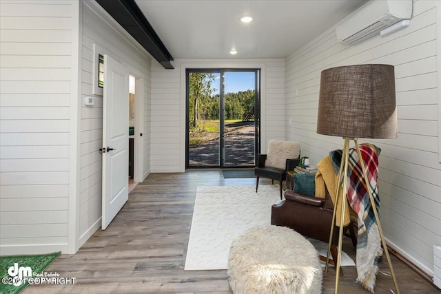 living area featuring wooden walls, light hardwood / wood-style floors, beam ceiling, and a wall unit AC