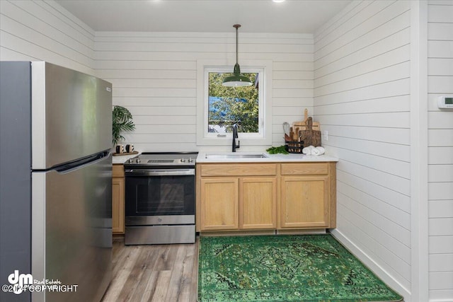 kitchen featuring sink, wood walls, decorative light fixtures, appliances with stainless steel finishes, and light wood-type flooring