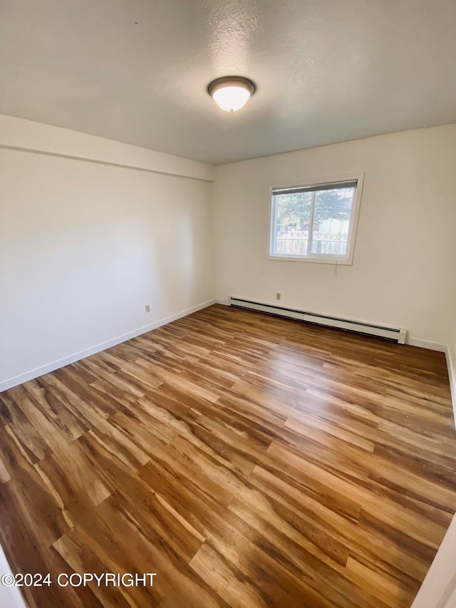 spare room with hardwood / wood-style floors and a baseboard heating unit