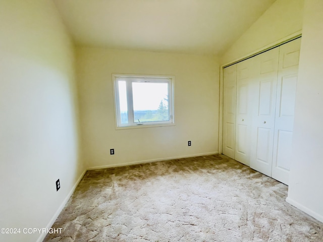 unfurnished bedroom featuring lofted ceiling, light colored carpet, and a closet