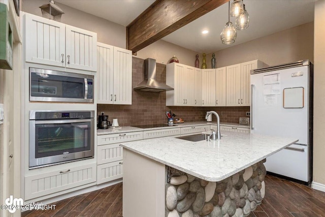 kitchen with wall chimney range hood, sink, a breakfast bar, appliances with stainless steel finishes, and an island with sink