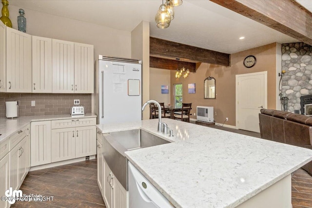 kitchen with beamed ceiling, decorative backsplash, fridge, a kitchen island with sink, and light stone countertops